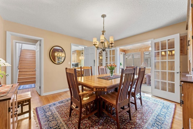 dining room featuring a chandelier, stairs, a textured ceiling, light wood finished floors, and baseboards