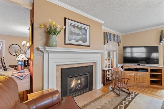living room with a textured ceiling, wood finished floors, a chandelier, crown molding, and a glass covered fireplace