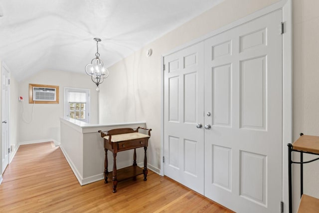 entryway featuring an AC wall unit, vaulted ceiling, light wood-style floors, baseboards, and a chandelier