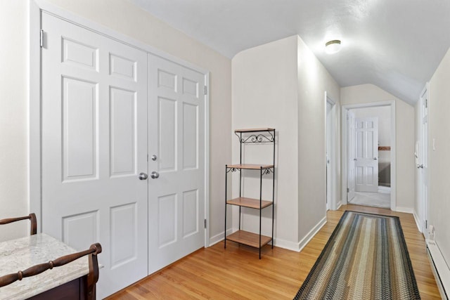 corridor with light wood-style flooring, baseboards, vaulted ceiling, and a baseboard heating unit