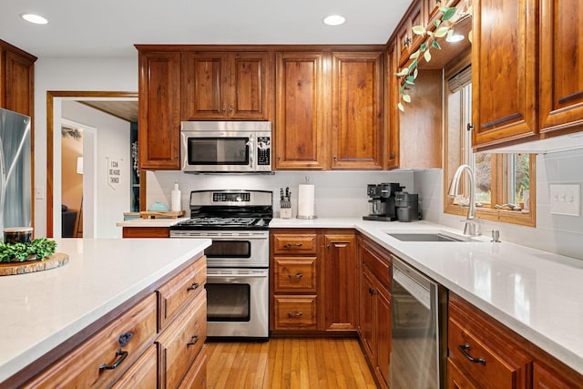 kitchen featuring stainless steel appliances, a sink, light countertops, light wood-type flooring, and recessed lighting