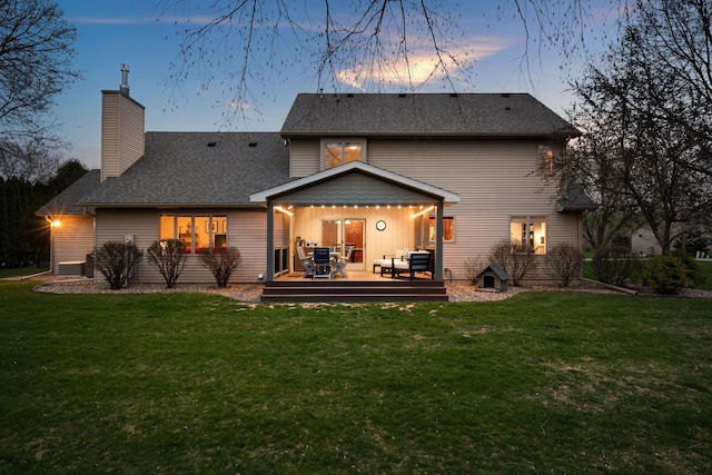 back of property with a lawn, a deck, a chimney, and roof with shingles