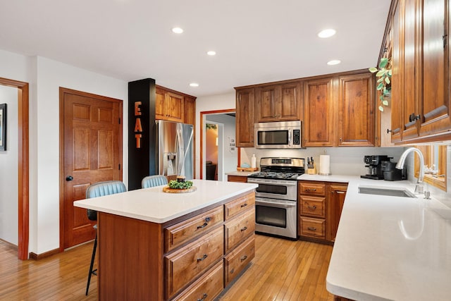kitchen featuring stainless steel appliances, a sink, light wood-style flooring, a kitchen bar, and recessed lighting