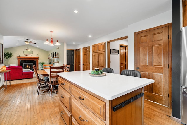 kitchen with ceiling fan, light wood finished floors, a warm lit fireplace, a center island, and recessed lighting
