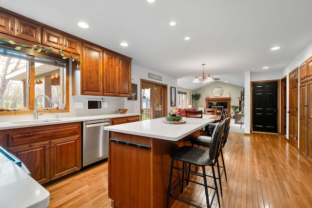 kitchen with dishwasher, a sink, light wood-style floors, a kitchen island, and light countertops
