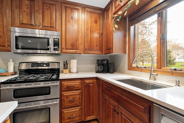 kitchen featuring stainless steel appliances, a sink, backsplash, light countertops, and brown cabinetry