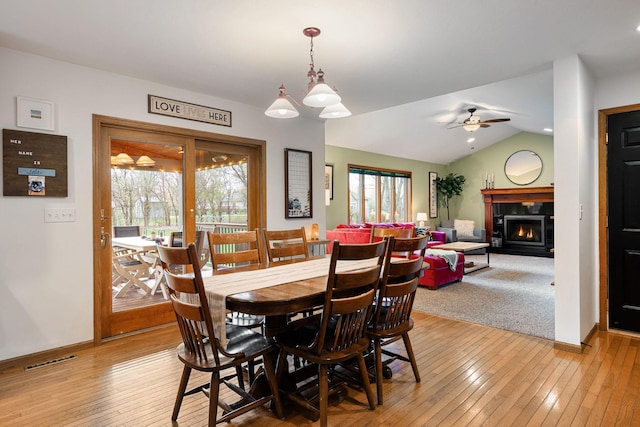dining space with a warm lit fireplace, light wood-type flooring, baseboards, lofted ceiling, and a ceiling fan