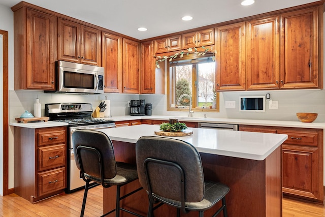 kitchen with stainless steel appliances, a sink, light countertops, brown cabinets, and a breakfast bar