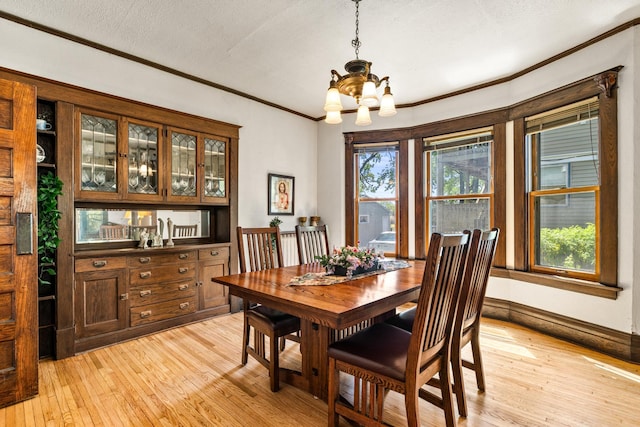 dining space with a chandelier, light wood-type flooring, ornamental molding, a textured ceiling, and baseboards