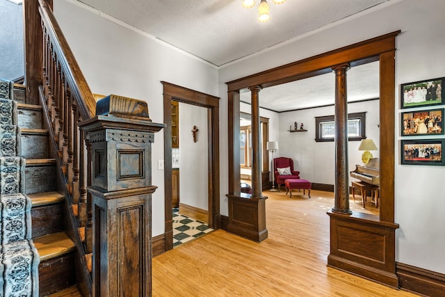 hall with light wood-type flooring, ornamental molding, ornate columns, baseboards, and a textured ceiling