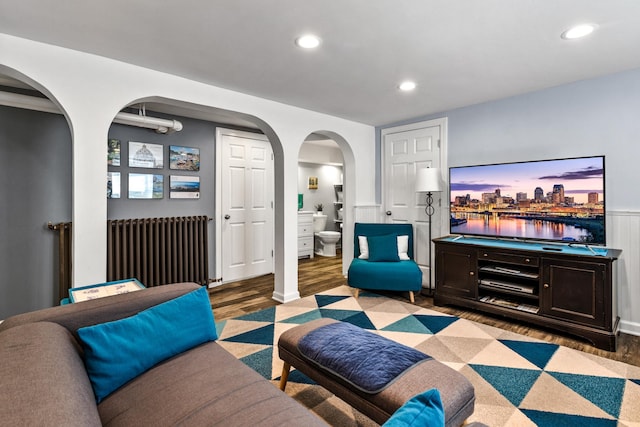 living area featuring radiator heating unit, arched walkways, wood finished floors, and recessed lighting