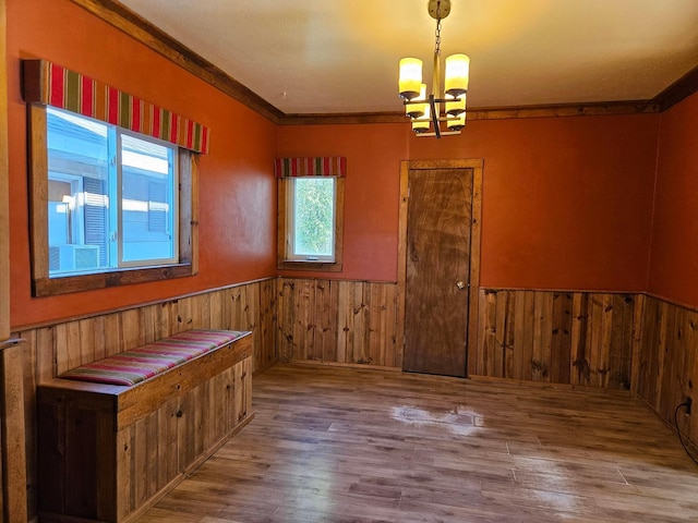 empty room with a wainscoted wall, a chandelier, wood finished floors, wooden walls, and crown molding