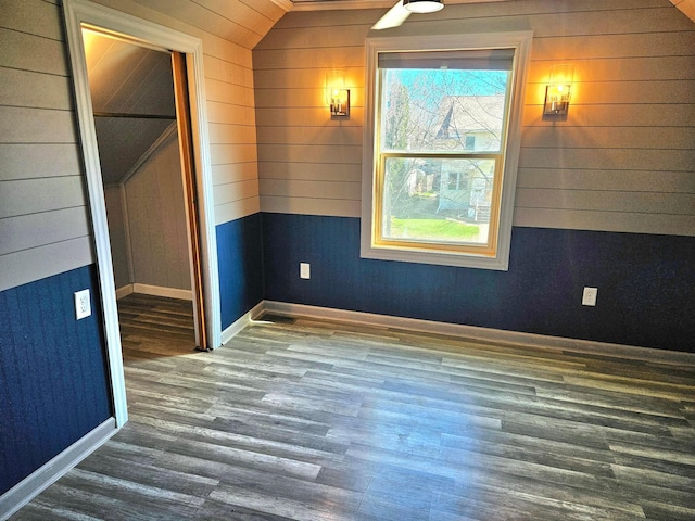 spare room featuring healthy amount of natural light, wood finished floors, lofted ceiling, wood walls, and baseboards