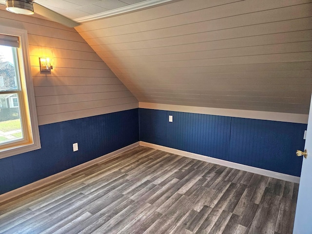 bonus room with plenty of natural light, vaulted ceiling, wood walls, baseboards, and wood finished floors
