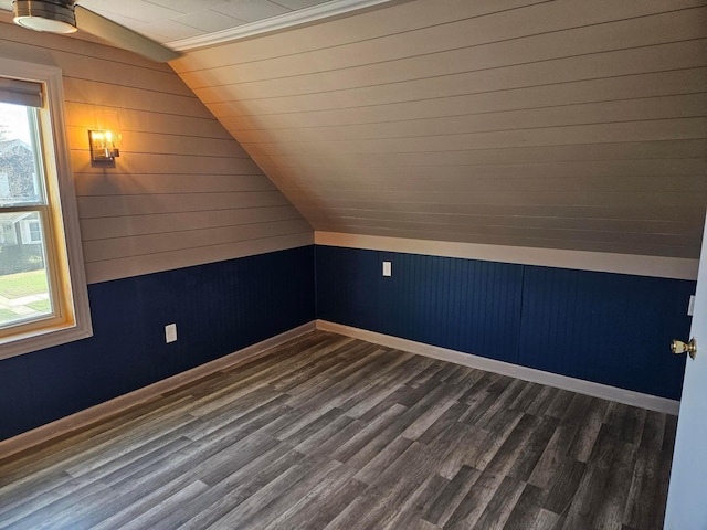 additional living space featuring vaulted ceiling, wooden walls, dark wood-type flooring, and baseboards