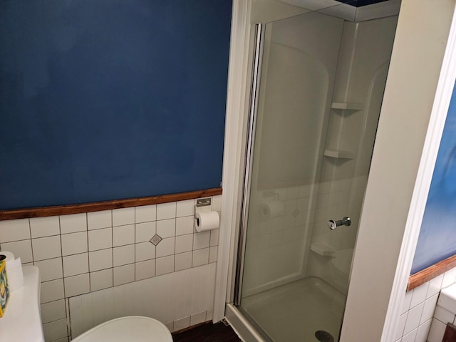 bathroom featuring tile walls, a shower stall, a wainscoted wall, and toilet