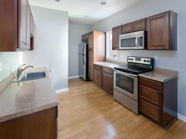 kitchen featuring appliances with stainless steel finishes, a sink, light wood-style floors, and baseboards