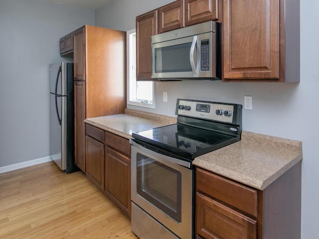 kitchen with appliances with stainless steel finishes, light wood-style floors, light countertops, and baseboards
