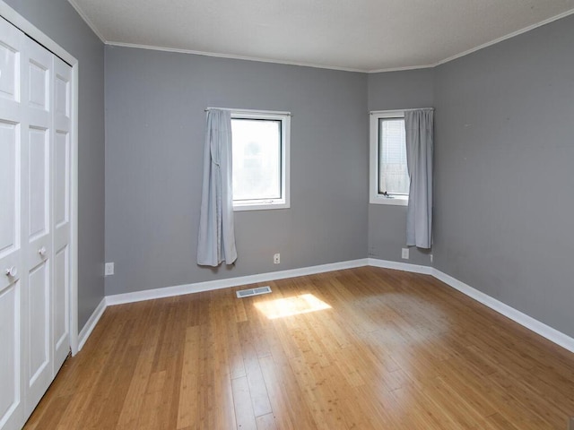 unfurnished bedroom with multiple windows, wood finished floors, crown molding, and baseboards