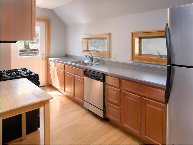 kitchen with stainless steel appliances, a sink, light wood-style floors, vaulted ceiling, and brown cabinetry