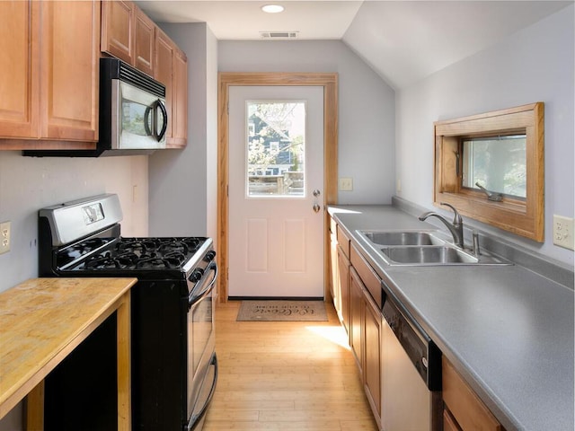 kitchen with appliances with stainless steel finishes, a sink, light wood-type flooring, lofted ceiling, and recessed lighting