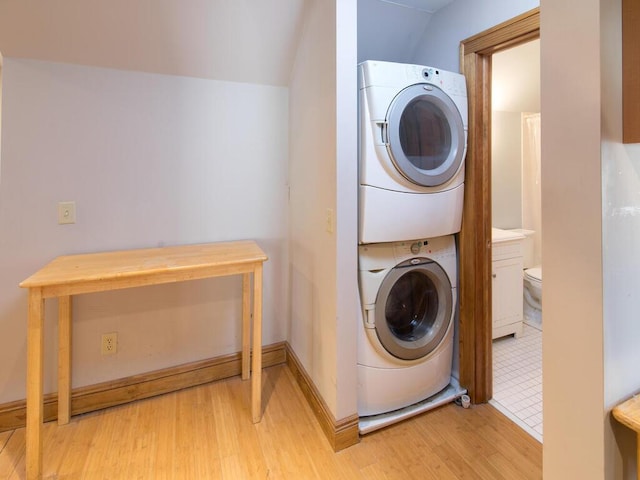 laundry area with estacked washer and dryer, light wood-style flooring, and baseboards