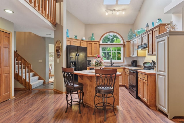 5662 Donegal Dr, Shoreview, MN 55126 - kitchen with black / electric stove, wood finished floors, a kitchen bar, a center island, and a skylight