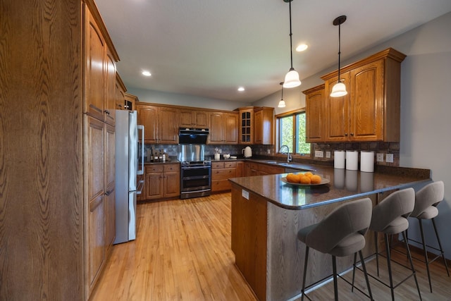 kitchen featuring appliances with stainless steel finishes, a peninsula, brown cabinets, a sink, and dark countertops