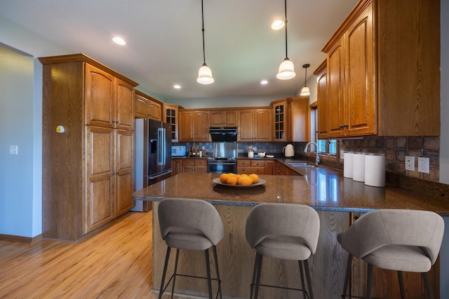 kitchen with appliances with stainless steel finishes, a sink, brown cabinetry, a peninsula, and glass insert cabinets