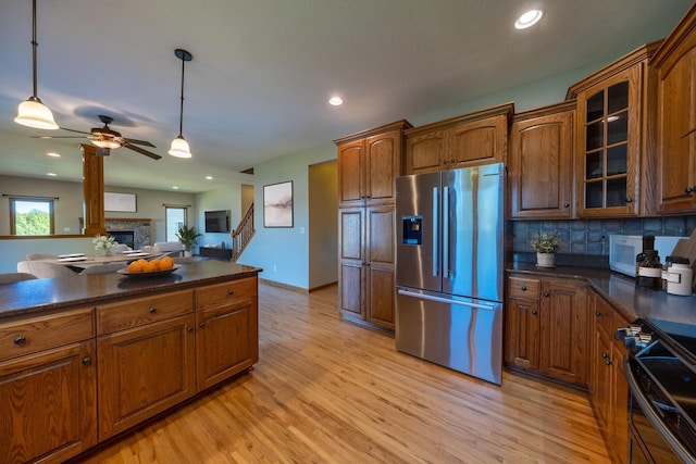 kitchen featuring stainless steel refrigerator with ice dispenser, dark countertops, range, a ceiling fan, and light wood-type flooring