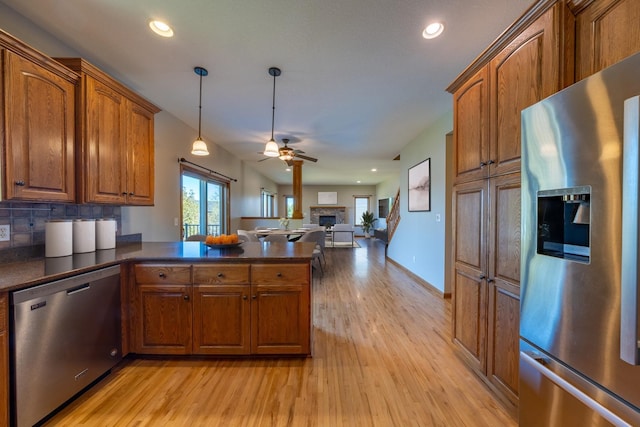 kitchen featuring appliances with stainless steel finishes, brown cabinets, a peninsula, dark countertops, and recessed lighting