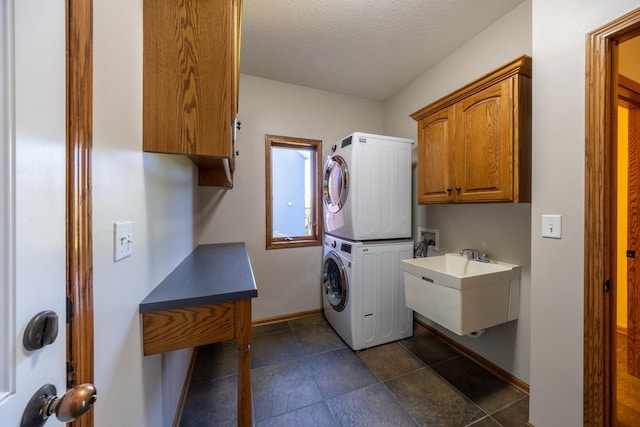 clothes washing area featuring stacked washer / drying machine, cabinet space, baseboards, and a textured ceiling
