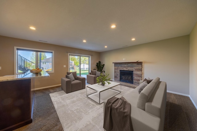 living area featuring dark carpet, baseboards, recessed lighting, and a stone fireplace