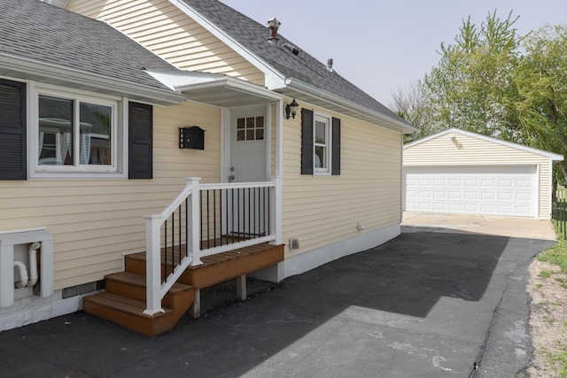 entrance to property with a detached garage and roof with shingles