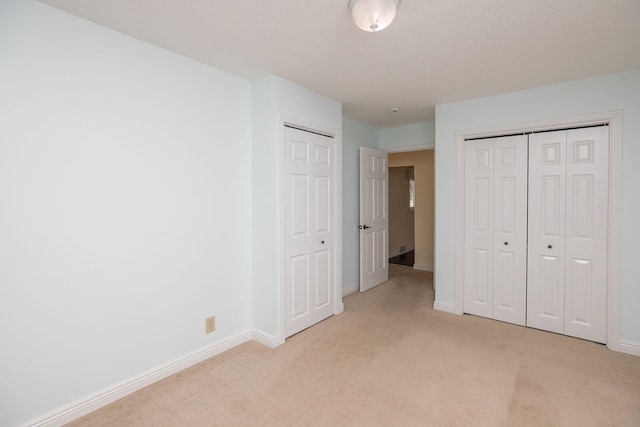 unfurnished bedroom featuring two closets, light carpet, and baseboards