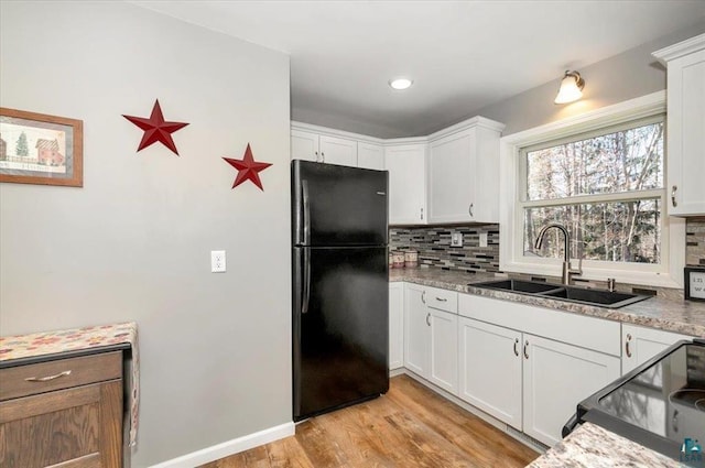 kitchen with black appliances, a sink, tasteful backsplash, light wood-type flooring, and white cabinets