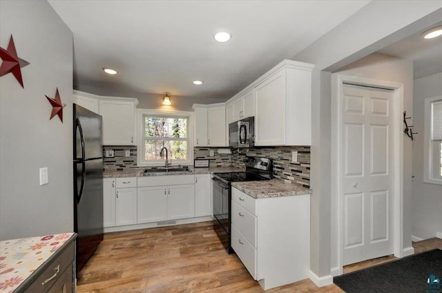 kitchen with black appliances, a sink, decorative backsplash, white cabinetry, and light wood-style flooring