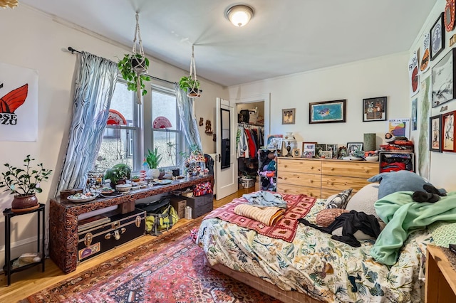 bedroom featuring wood finished floors, ornamental molding, and a spacious closet