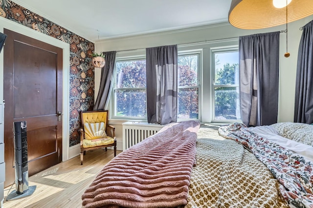 bedroom with radiator heating unit, ornamental molding, wood finished floors, baseboards, and wallpapered walls