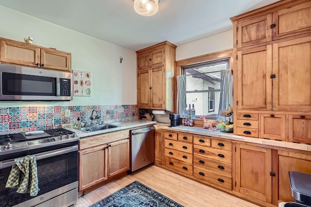 kitchen with appliances with stainless steel finishes, light wood-style flooring, light countertops, a sink, and backsplash
