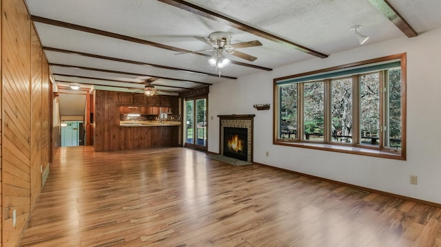 unfurnished living room featuring beamed ceiling, light wood finished floors, ceiling fan, a fireplace, and a textured ceiling