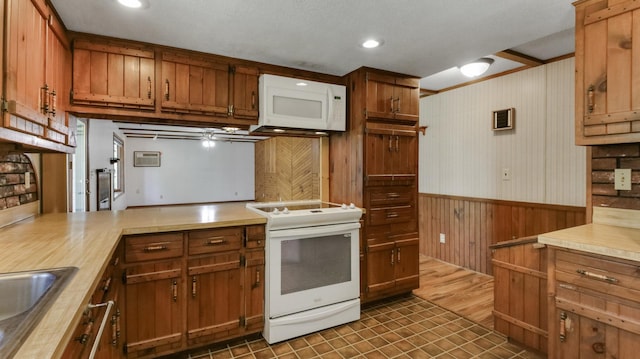 kitchen with white appliances, a wainscoted wall, light countertops, wooden walls, and brown cabinets