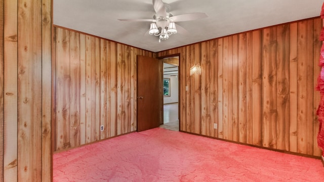 carpeted spare room with ceiling fan and wood walls