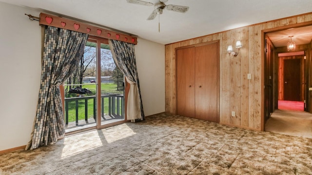 carpeted empty room featuring wooden walls, ceiling fan, and baseboards