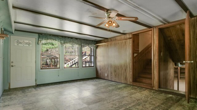 unfurnished living room with a ceiling fan, stairs, wooden walls, and tile patterned floors