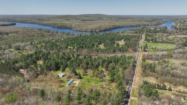 aerial view of property and surrounding area with a nearby body of water and a heavily wooded area