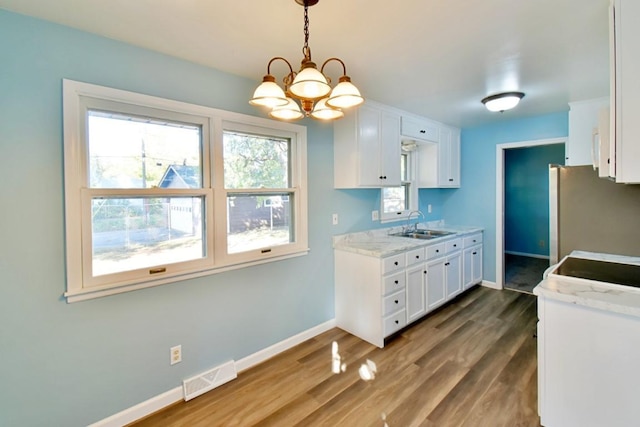 kitchen featuring freestanding refrigerator, white cabinets, a chandelier, wood finished floors, and baseboards