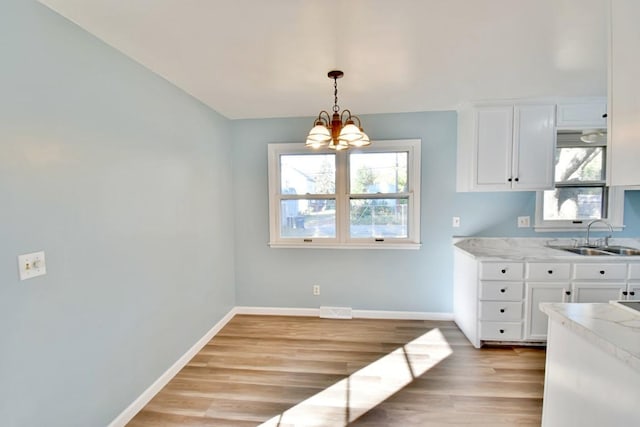 kitchen featuring a sink, a chandelier, light wood-style floors, white cabinetry, and baseboards