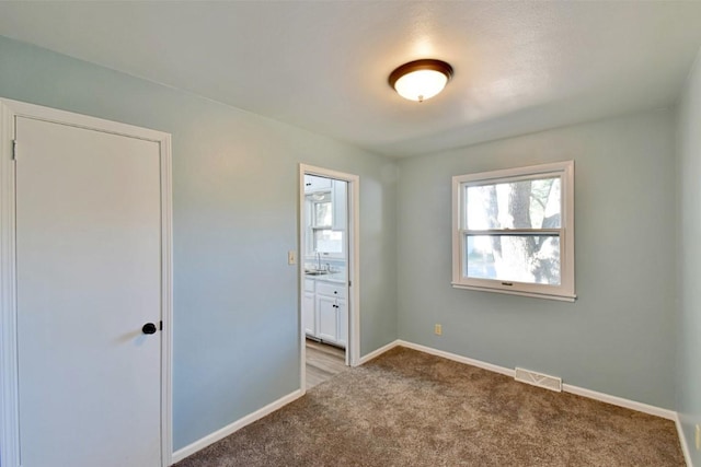 unfurnished bedroom with light carpet, multiple windows, baseboards, and connected bathroom