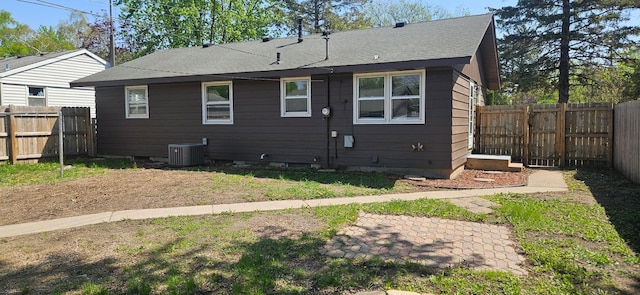back of house with central AC unit, a fenced backyard, and a shingled roof